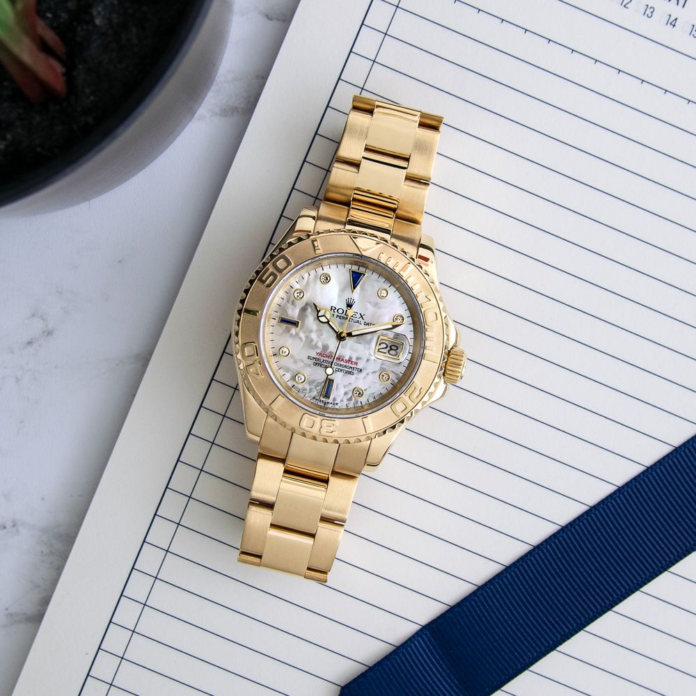 A top down photo of the Rolex Yacht-Master 16628 in 18k Yellow Gold with a Mother of Pearl Sapphire Diamond Dial on a notebook